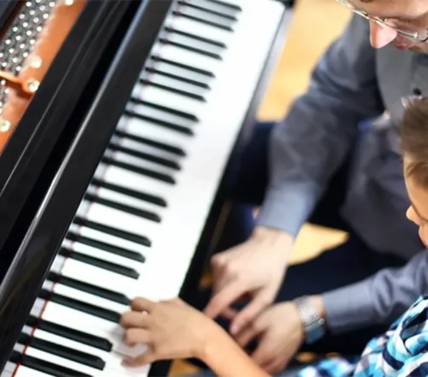 a boy learning piano from a man