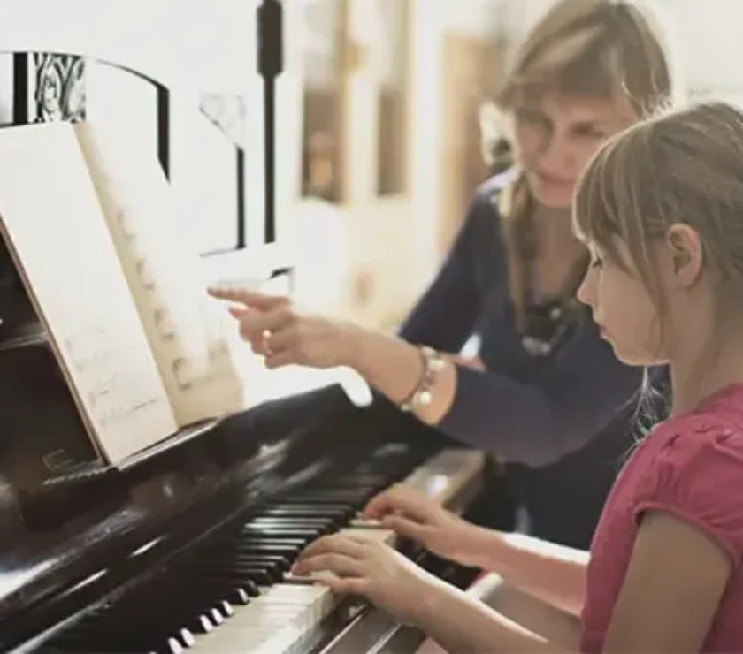 a little girl is learning piano with a women