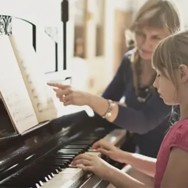 a little girl is learning piano with a women